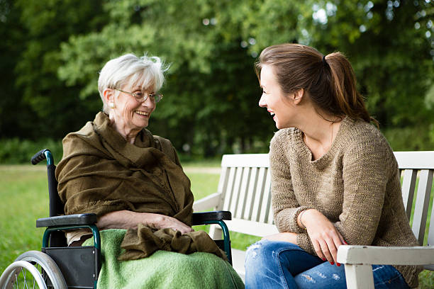 young and disabled senior woman have a talk in park charming young woman and senior woman in a  wheelchair sit together in a park and have fun senior adult women park bench 70s stock pictures, royalty-free photos & images