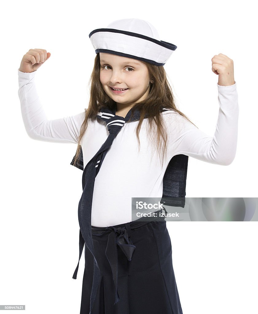 Sailor Girl Portrait of little girl dressed as a sailor standing with raised arms, flexing her muscles and smiling at the camera. Studio shot, isolated on white. Child Stock Photo