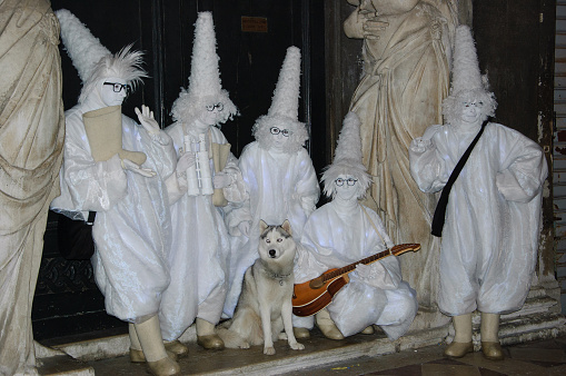 Venice, Italy - February 13, 2015: Group of mimes in Pierrot costumes and their dog at San Marco square in the evening dark. he Carnival in Venice is annual event which ends on Shrove Tuesday.