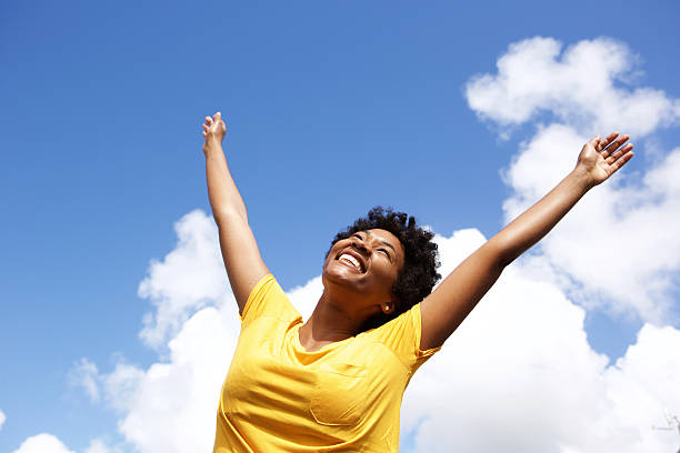 Cheerful young woman with hands raised towards sky Portrait of cheerful young woman standing outside with her hands raised towards sky excited woman yellow stock pictures, royalty-free photos & images