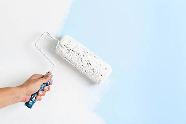 Close up of painter arm painting a wall with paint roller; copy space