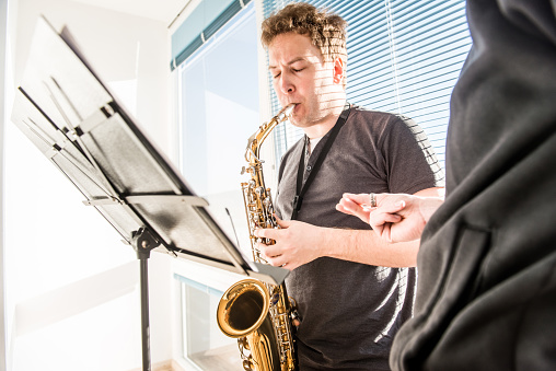 Young man learning how to play saxophone at home, teacher supervising the student, close up