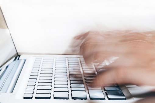 Close-up of Human Hands typing on laptop in blurred motion with copy space above (selective focus) - blurred caused is intended to make fingers look moving fast