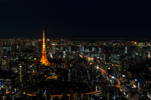 Cityscape of Tokyo at night, as seen from the top of one of the highest buildings in Roppongi Hills, with the illuminated Tokyo Tower glowing in the dark. Long exposure.