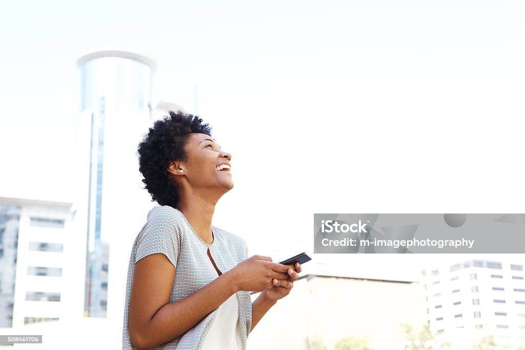 Smiling african woman standing outside holding cell phone Portrait of a smiling african american woman standing outside holding cell phone Looking Up Stock Photo