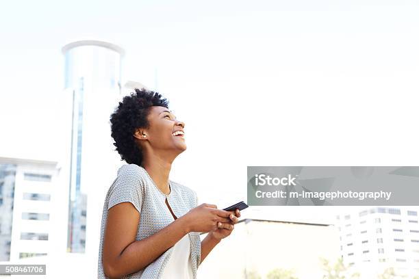 Smiling African Woman Standing Outside Holding Cell Phone Stock Photo - Download Image Now