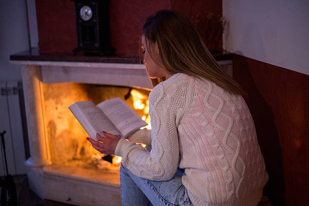 istock woman reading a book by fireplace 508466604