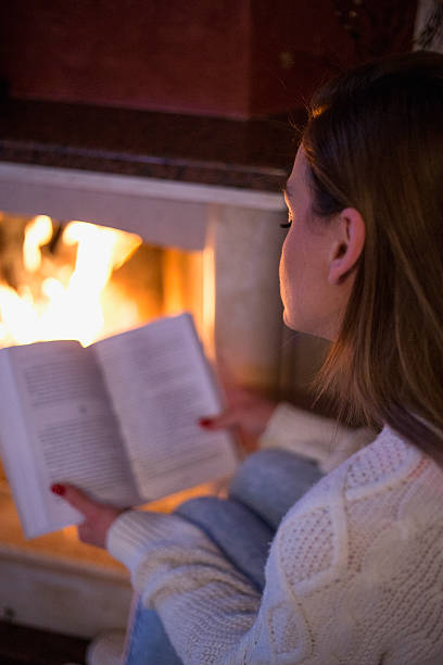 istock woman reading a book by fireplace 508466678