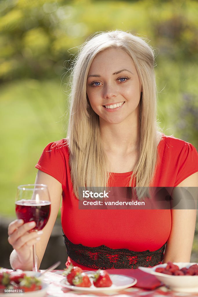 Picnic: Girl In A Red Dress Cute strawberry-blonde girl wearing a red dress enjoying a glass of wine and some Summer fruit at a picnic. 18-19 Years Stock Photo