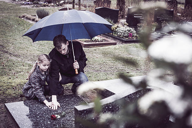Father and daughter at graveyard visiting grave of mother