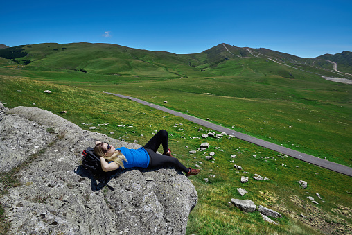 woman lying on mountain peak with her hands behind her head, enjoying moment of silence in nature.