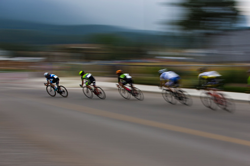 A group of male bicycle racers ride together during a criterium road bike race.  A criterium road bike race is an event where competitors do several laps around a closed circuit usually in a city or urban center.