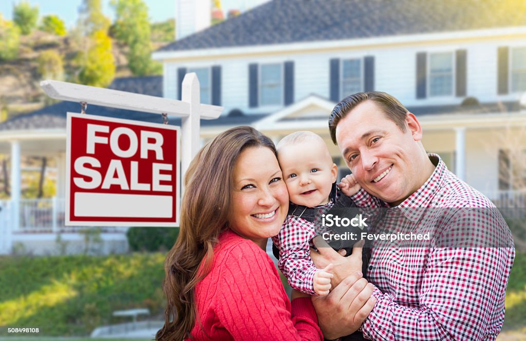 Young Family In Front of For Sale Sign and House Happy Young Family In Front of For Sale Real Estate Sign and House. Home Ownership Stock Photo