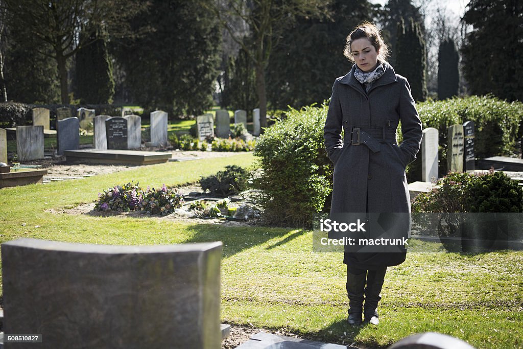 Woman standing at grave Woman sitting at grave with hands in pockets Funeral Stock Photo