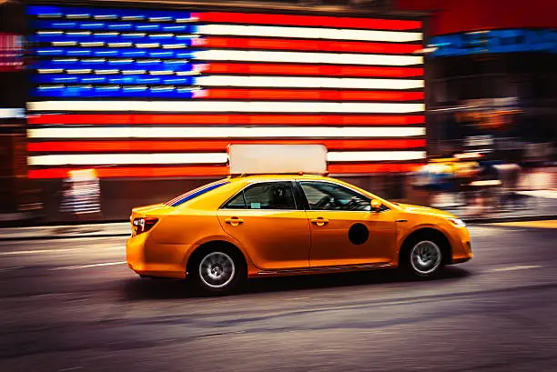 Taxi goes fast in front of USA flag - Times Square, New York