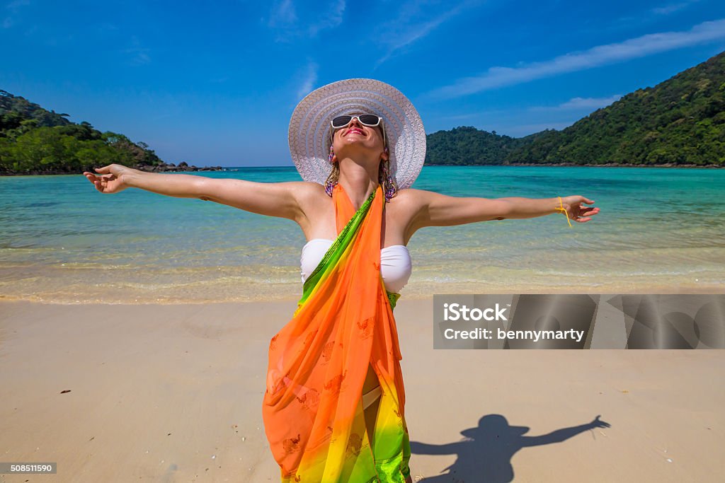Happy woman on tropical beach Happy and attractive woman with yellow sarong and white wide-brimmed hat on tropical beach of Koh Surin Nuea, North Surin Island National Park, Phang Nga, Andaman Sea, Thailand Sarong Stock Photo