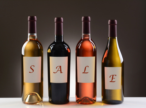 Four Wine Bottles with their labels spelling out the word SALE on a light to dark gray background. Four different wines including: Cabernet Sauvignon, Chardonnay, Sauvignon Blanc, and White Zinfandel.