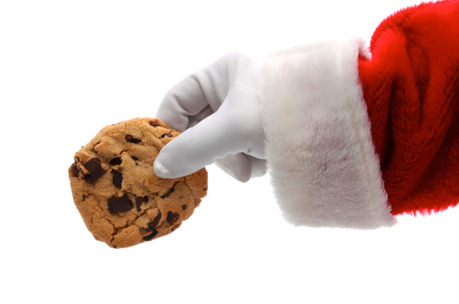 Closeup of Santa Claus holding a chocolate chip cookie in his hand. Horizontal format isolated over a white background, showing Santa's hand and arm only.
