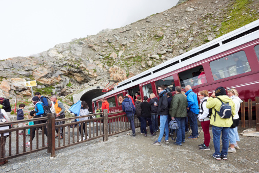 Saint-Gervais-les-Bains, France - August 15, 2014: tourists alight from the train at the Nid d'Aigle terminus on a foggy summer day. In the scene also people queuing for boarding the train.