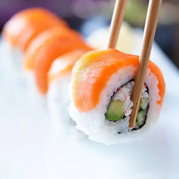 picking up a piece of sushi with chopsticks, shot with selective focus on sushi being picked up