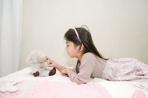 A little girl fondly plays with her stuffed toy. She's alone with her toy on her bed, and is showing affection like it's her best friend. She could be saying good-bye to her toy.