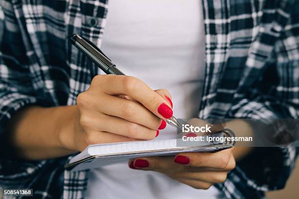 Woman In Plaid Shirt And A Red Manicure Pen Writing Stock Photo - Download Image Now