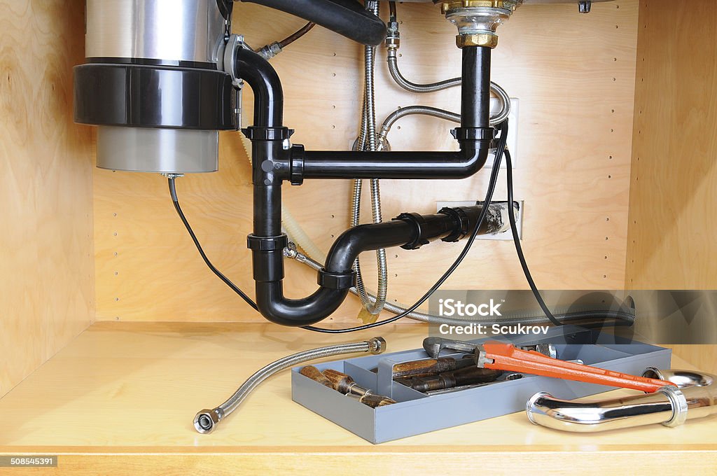 Under a Kitchen Sink Detail of the plumbing system under a modern kitchen sink, with a plumbers tool tray and equipment. Horizontal format. Sink Stock Photo