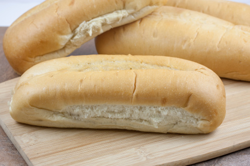 A selection of fresh sub or sandwich rolls on a wooden cutting board.