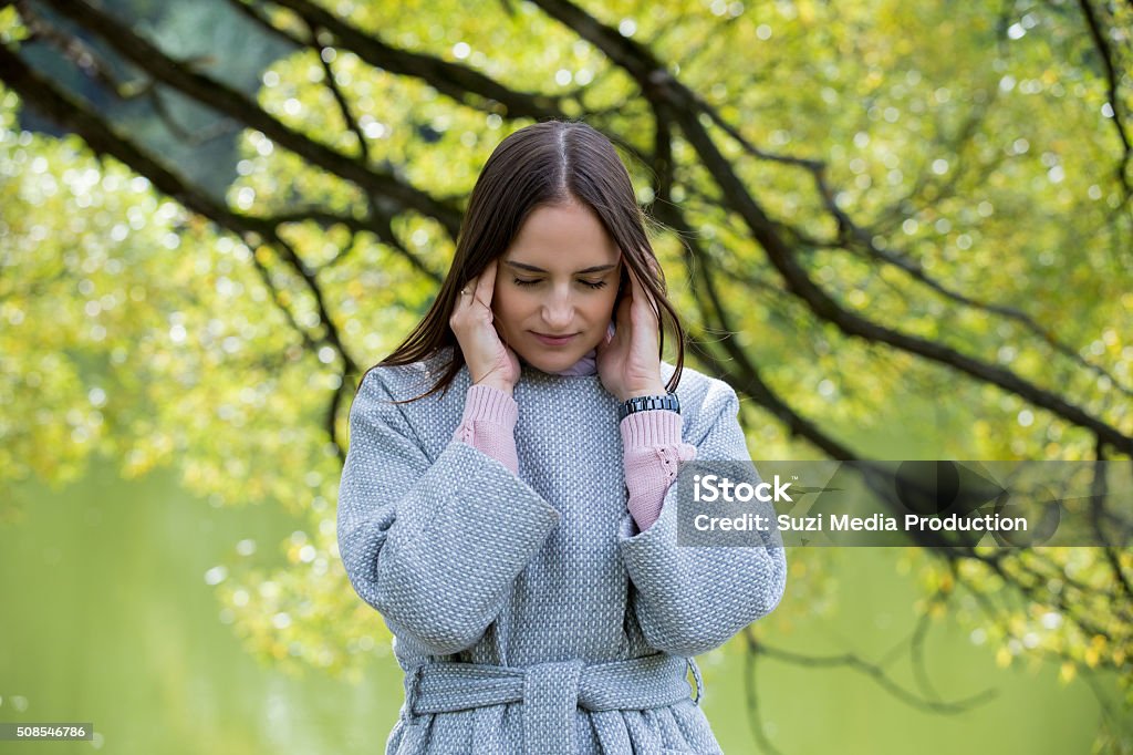 Woman with headache Young beautiful woman standing in the park, suffering from headache. Touching temples, having pain. Looking stressful. Adult Stock Photo