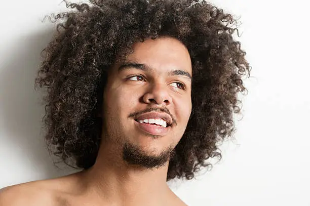 Close-up of a happy young man with curly hair looking away over white background