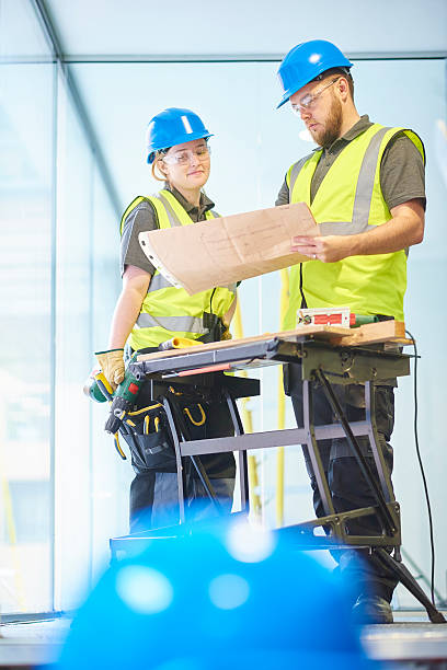 male and female carpenters checking the plans a teenage female carpenter is discussing a modern office refurbishment job with her co-worker whilst looking at the blueprints. The man is holding the blueprints to check where the partition walls are to be installed . They are wearing safety workwear. train air conditioner stock pictures, royalty-free photos & images
