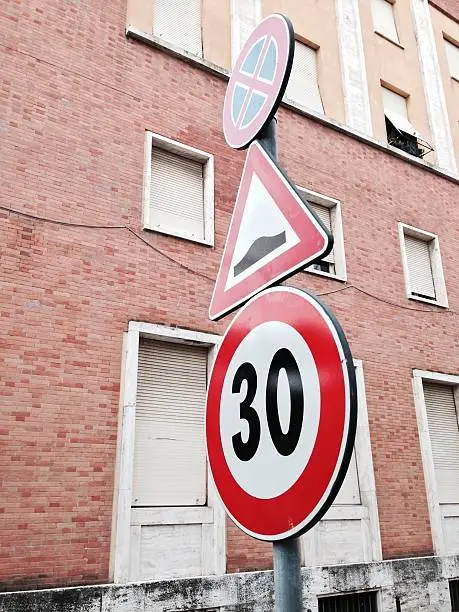 Three roadsigns with architectural background:a sped limit, a speed limiter warning, a no parking or stay sign