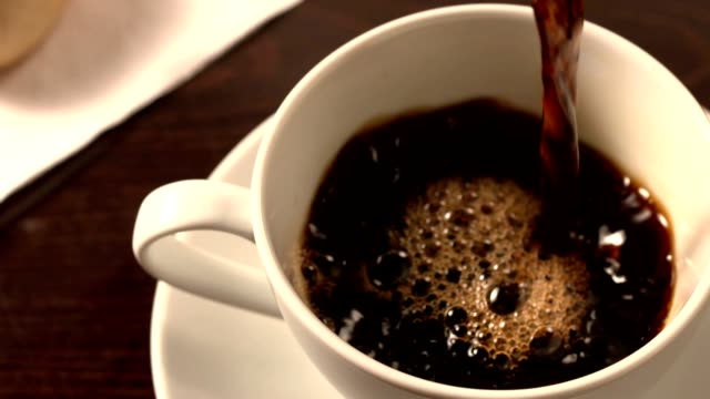 Black coffee pouring into cup with saucer