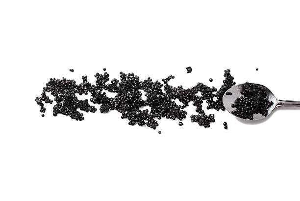 black caviar and spoon isolated on white background the eggs of caviar scattered on the surface. flat lay, top view sturgeon fish stock pictures, royalty-free photos & images