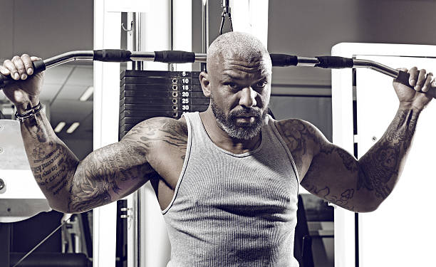 Tattooed middle aged bearded black man at a gym Tattooed middle aged bearded black man exercising on apparatus at a gym forearm tattoos men stock pictures, royalty-free photos & images