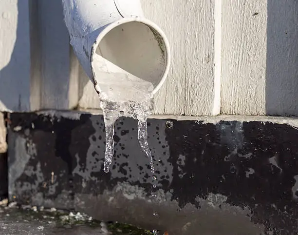 Icicles in Drainpipe with water drops falling from it.