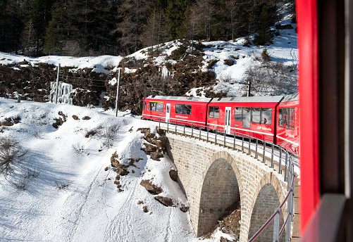Tirano, Italy, 14th January 2012 - Red train of Bernina, on the Retica railway, over a bridge during its climbing to reach Saint Moritz in the Swiss Alps.