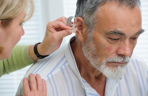 Doctor inserting hearing aid in senior's ear