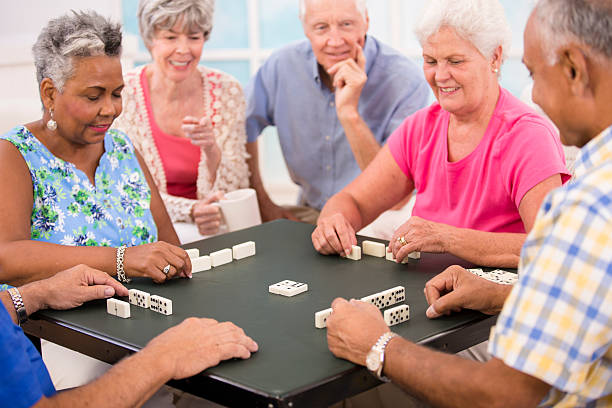 senior erwachsene freunde spielen domino spielten.  hause oder community center ambiente. - group of people aging process home interior indoors stock-fotos und bilder