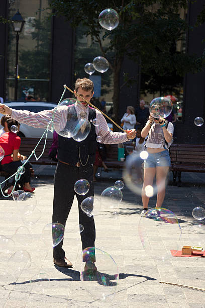 Bubble maker on Place d'Armes in Montreal Montreal, Quebec, Canada - July 11, 2014: Street performer making bubbles in the middle of place d'Armes in Old Montreal in Canada. Tourist is taking photos of huge bubbles made by the entertainer. place darmes montreal stock pictures, royalty-free photos & images