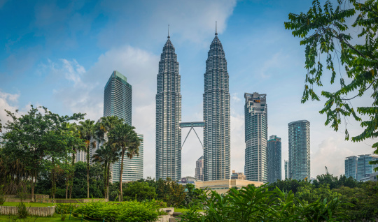 The gleaming spires of the Petronas Towers soaring over the leafy foliage of KLCC Park and the skyscrapers of downtown Kuala Lumpur, Malaysia's vibrant capital city. ProPhoto RGB profile for maximum color fidelity and gamut.