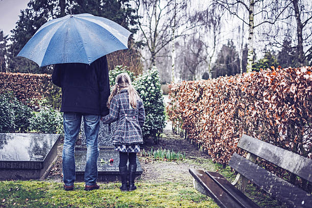 Father and daughter visiting gravestone of deceased mother Father and daughter visiting gravestone of deceased mother with umbrella on rainy day sad child standing stock pictures, royalty-free photos & images