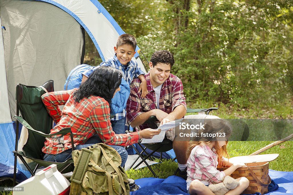 Family of four camping outdoors in forest. Tent, supplies. Latin family of four camping outdoors in a national park. Forest area with tent and supplies. 20-29 Years Stock Photo