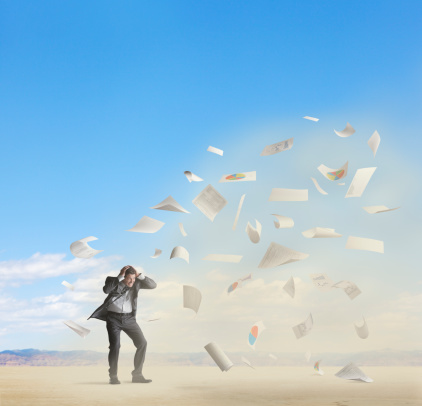 A businessman fighting through a sandstorm with a lot of paperwork being tossed in the air.