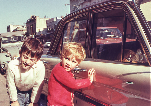 photo from the seventies of two children next to a car in the street.
