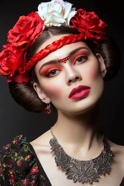Beautiful young woman with bright red make up looking like Frida Kahlo. Over black background