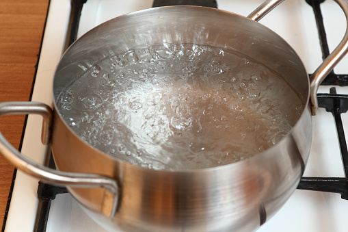 Boiling water into saucepan. Cooking buckwheat groats on gas stove.