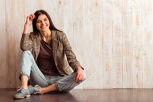 Beautiful girl in casual clothes looking in camera and smiling while sitting against wooden background