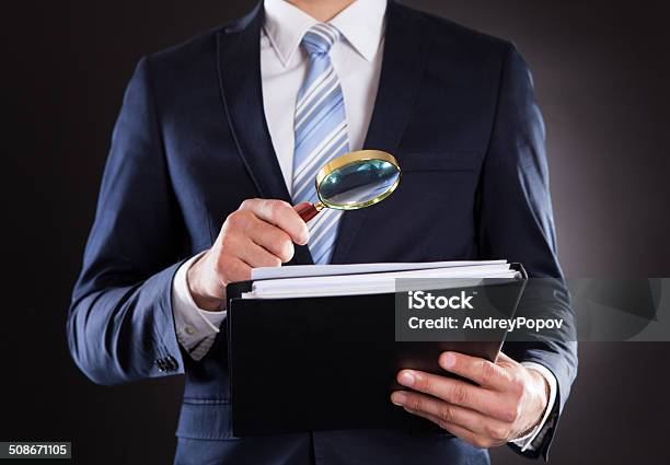 Businessman Examining Documents With Magnifying Glass Stock Photo - Download Image Now