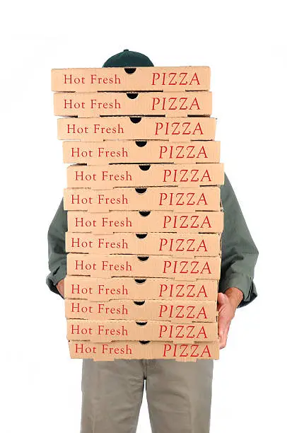 A Deliveryman hidden behind a large stack of pizza boxes he is carrying. Vertical format over white.